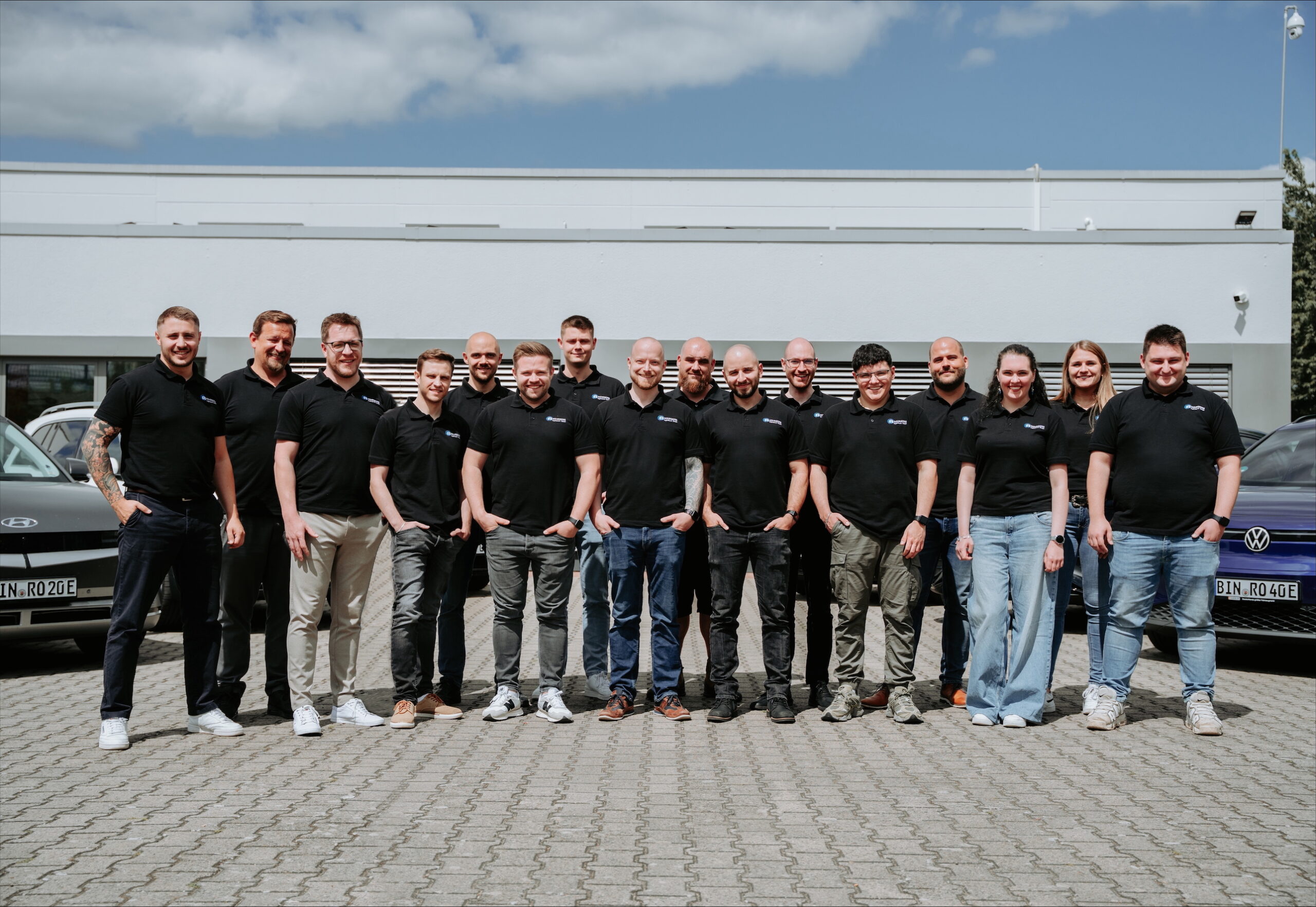 Ein Gruppenfoto von den Mitarbeitern von Rohrberg Ingenieure GmbH. Zu sehen sind 16 Personen, die größtenteils lächeln. Im Hintergrund ist noch der Fuhrpark der Firma zu erkennen.