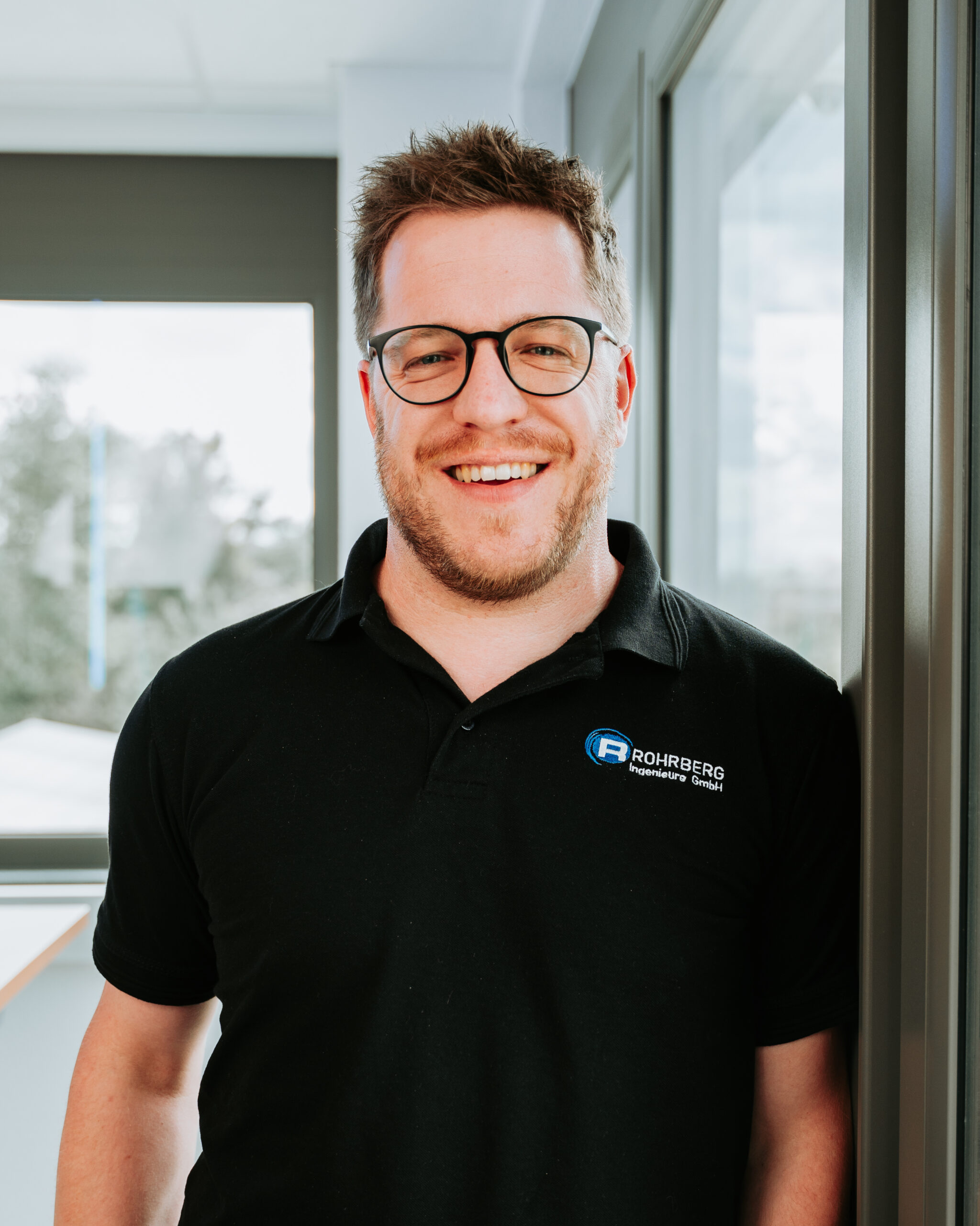 Ein Portrait des Geschäftsführers von Rohrberg Ingenieure. Die Person lächelt in die Kamera und trägt dunkle Kleidung und hat die Arme verschränkt.